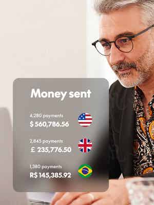 A man works on his laptop computer with an overlay of a Money Sent screen showing denominations from the USA, the UK, and Brazil. 