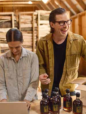 Two people in a workroom packing bottles into a box.